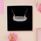 A wooden and glitter acrylic necklace with gold chain in a black box of a cute family of ducks two adult white ducks and four yellow ducklings playing and splashing in the water