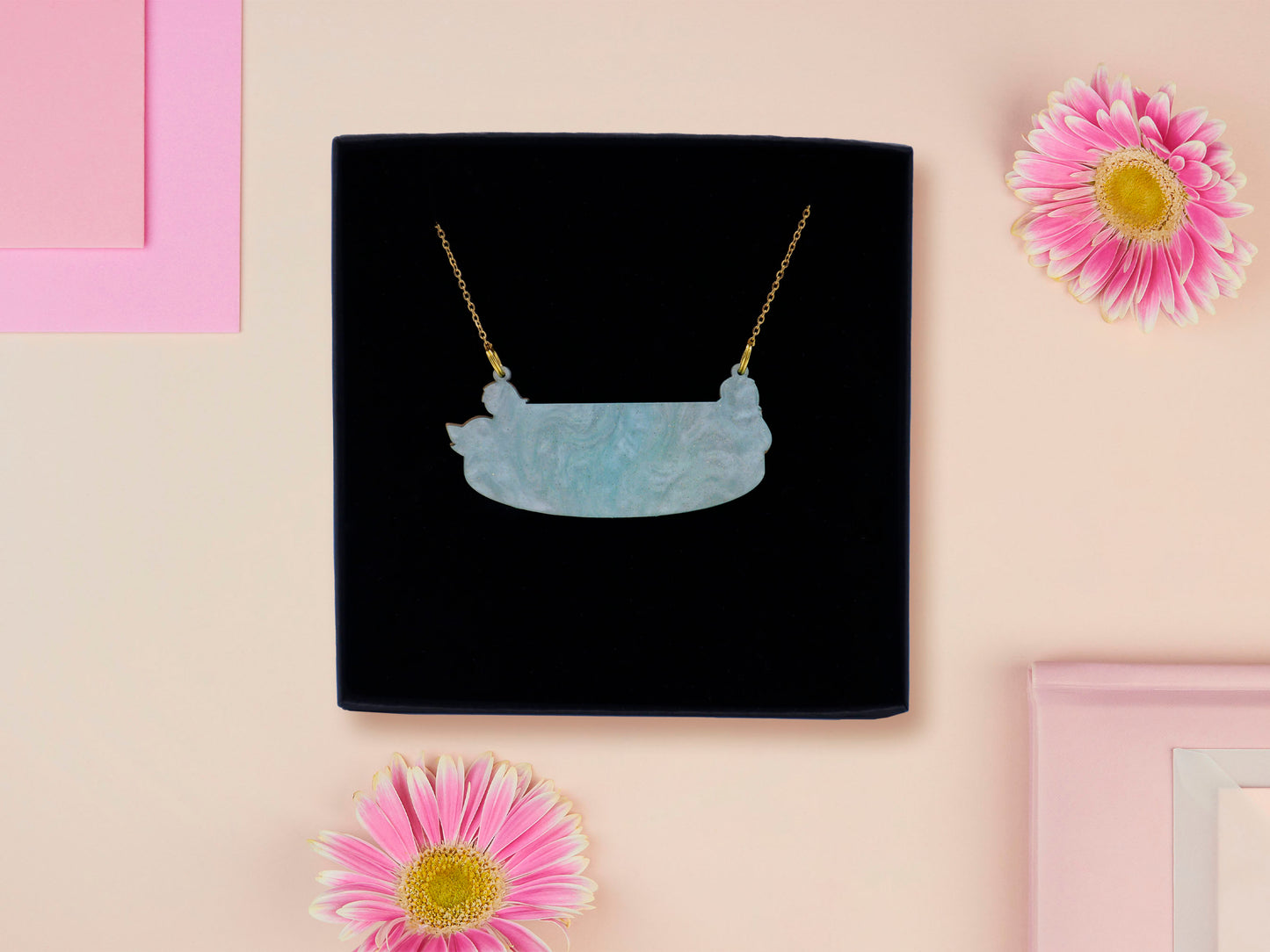 A wooden and glitter acrylic necklace with gold chain in a black box of a cute family of ducks two adult white ducks and four yellow ducklings playing and splashing in the water