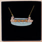 A wooden and glitter acrylic necklace with gold chain in a black box of a cute family of ducks two adult white ducks and four yellow ducklings playing and splashing in the water