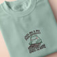 An embroidered green t-shirt design of a cute frog happily looking at his binder of tcg trading cards surrounded by the quote Just Me And My Shiny Cardboard Against The World