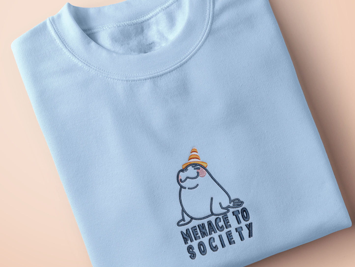 T-shirt with an embroidered blue design of a cute Neal the seal smuggly wearing an orange and white trafic cone with the quote meance to society
