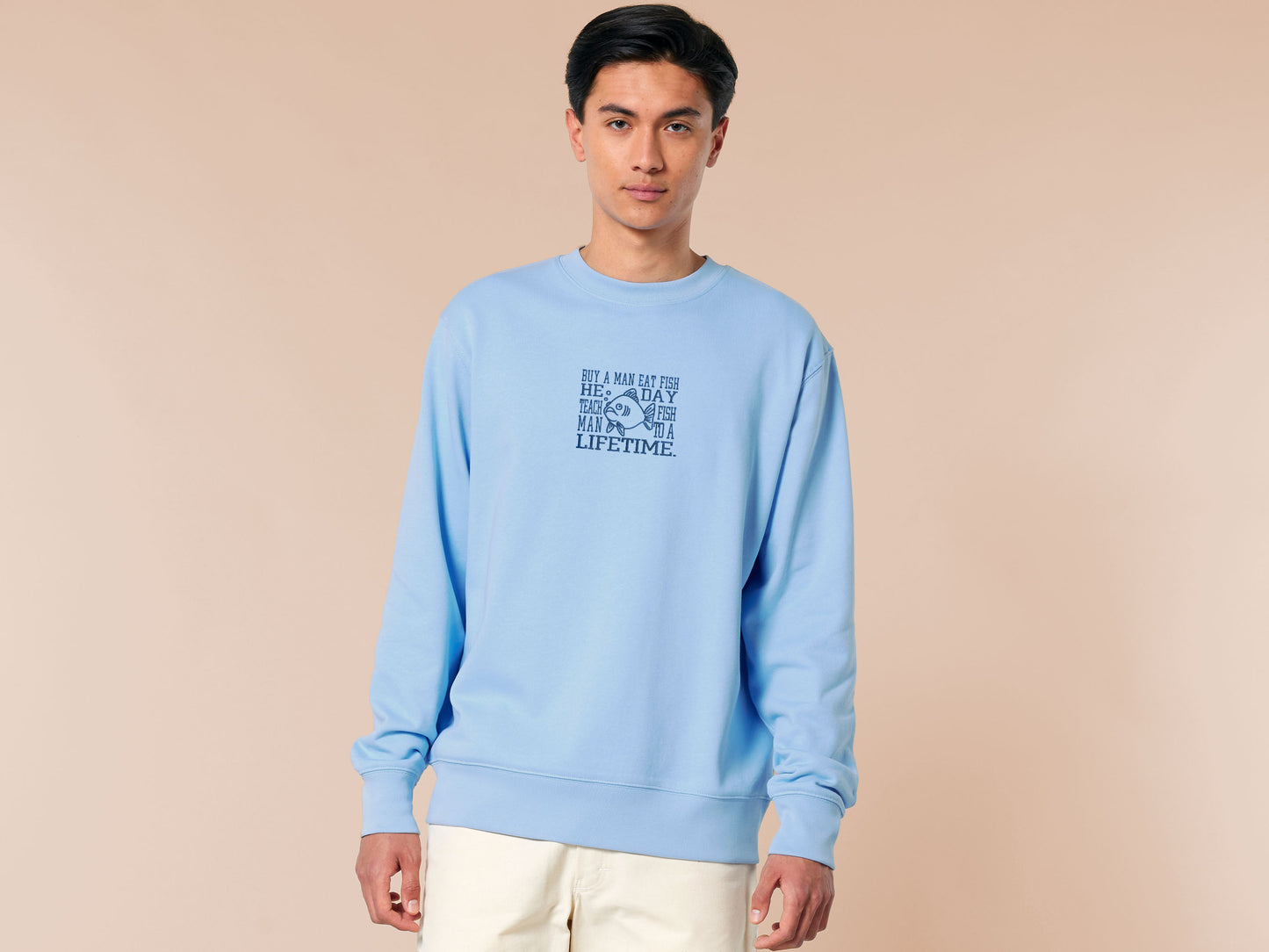 An embroidered blue sweater design of a funny cartoon fish and the text quote buy a man eat fish he day teach fish man to a lifetime.