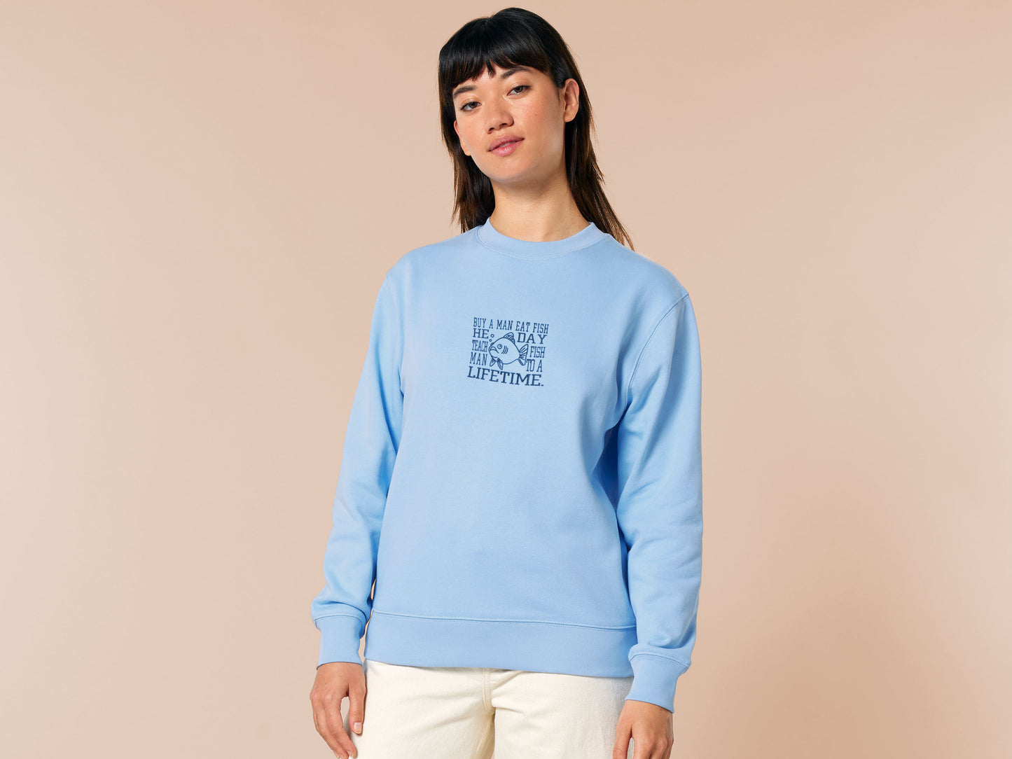 An embroidered blue sweater design of a funny cartoon fish and the text quote buy a man eat fish he day teach fish man to a lifetime.