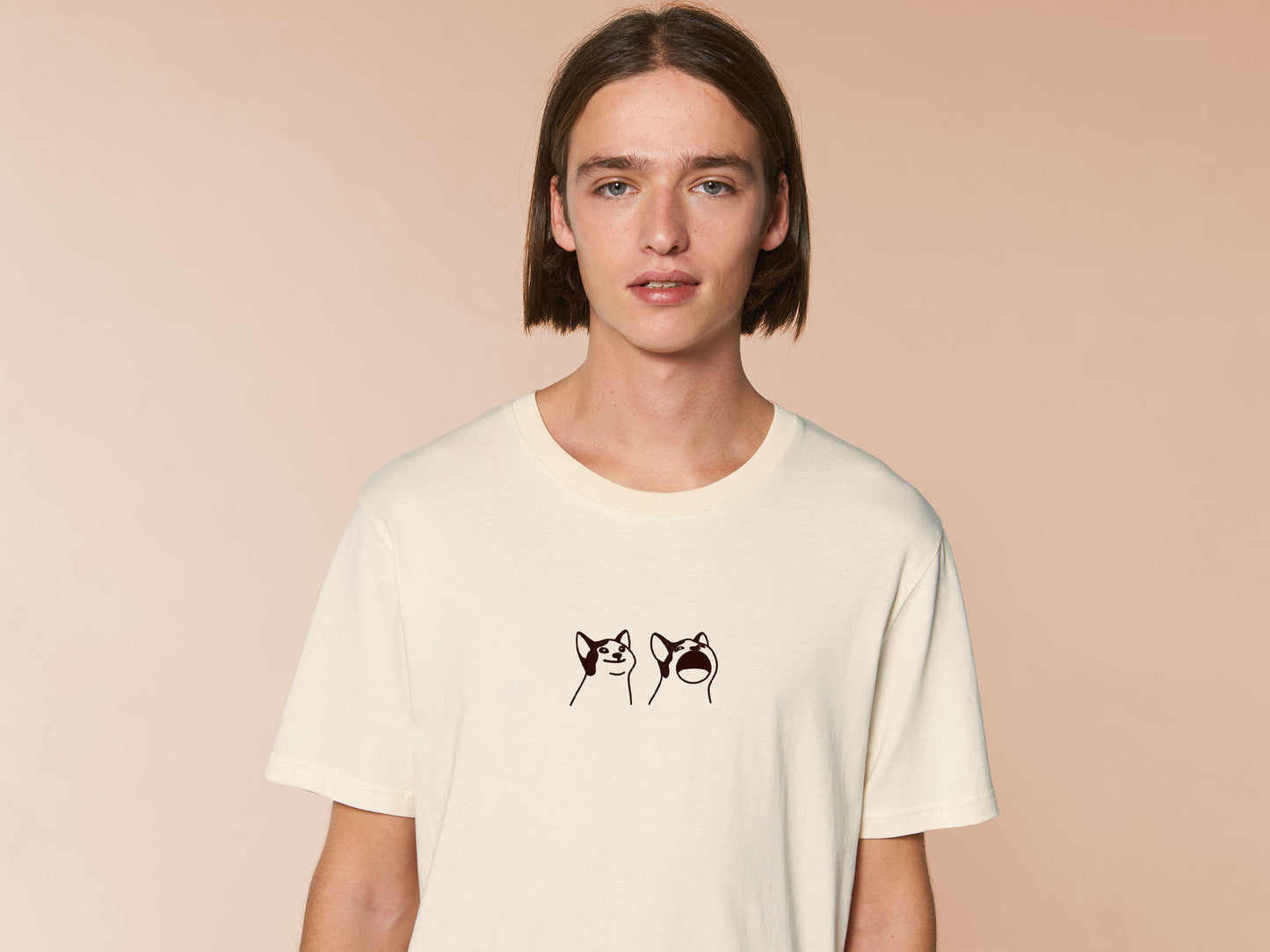 A man wearing a cream crew neck short sleeve t-shirt, with an embroidered brown thread design of a cute popcat the cat meme reaction twitch emote