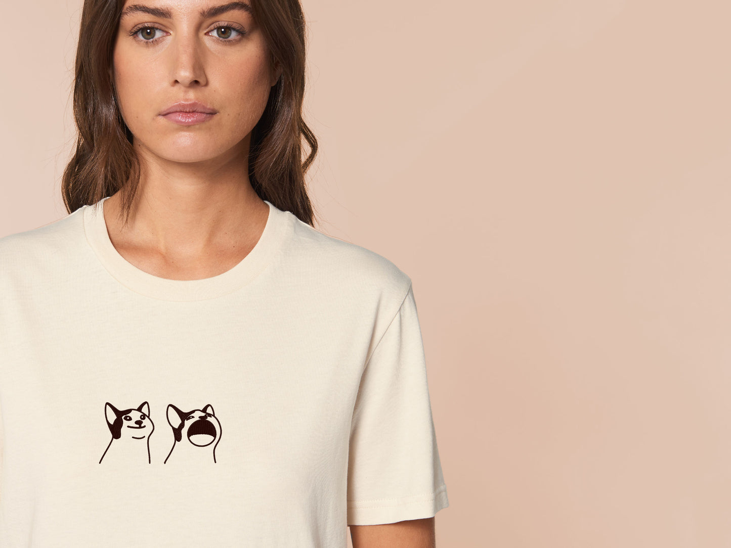 A woman wearing a cream crew neck short sleeve t-shirt, with an embroidered brown thread design of a cute popcat the cat meme reaction twitch emote