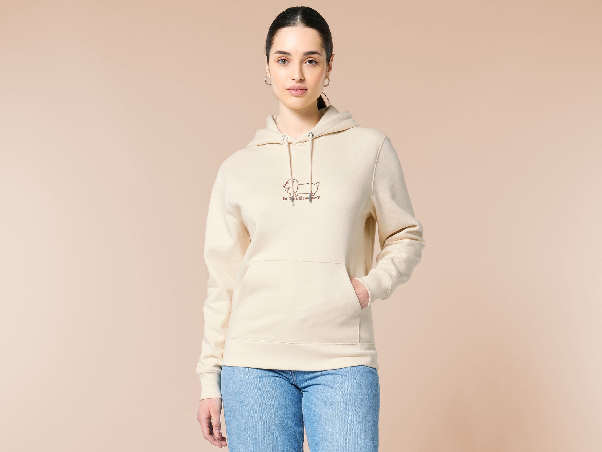 A cream crew neck long sleeve hoodie, with an embroidered brown thread design of a cute daschund dog looking concerend surrounded by the quote In This Economy?