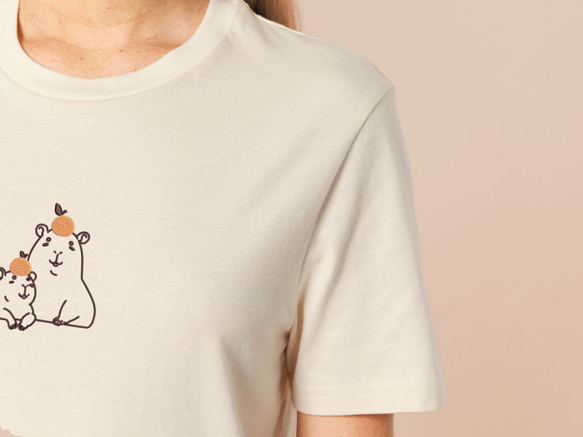 Embroidered cream t-shirt design of two cute chibi capybaras with oranges on their heads.