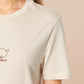 A cream crew neck short sleeve t-shirt, with an embroidered brown thread design of a cute daschund dog looking concerend surrounded by the quote In This Economy?