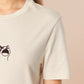 A cream crew neck short sleeve t-shirt, with an embroidered brown thread design of a cute popcat the cat meme reaction twitch emote