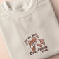 A cream crew neck short sleeve t-shirt, with an embroidered design of a cute shiba inu dog looking stressed surrounded by the quote Let Me Just Overthink This