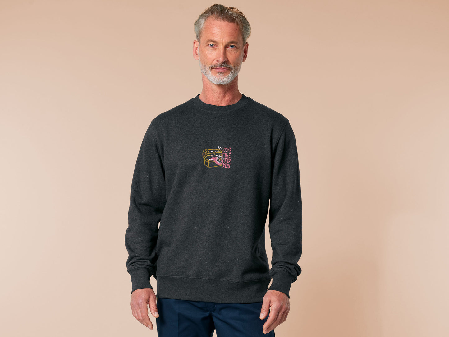 A dark grey crew neck long sleeve sweater, with an embroidered cute chibi mimic chest holding a D20 dice rolled a one and the quote Looks fine to you.