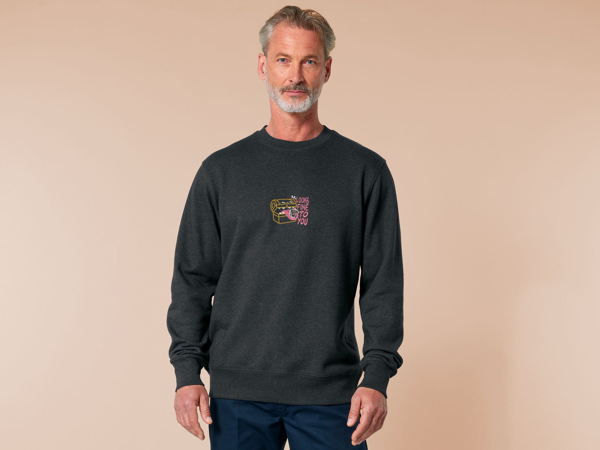 A dark grey crew neck long sleeve sweater, with an embroidered cute chibi mimic chest holding a D20 dice rolled a one and the quote Looks fine to you.