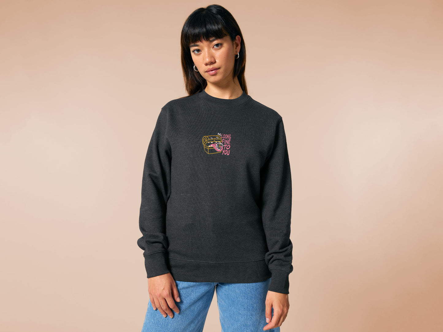 A dark grey crew neck long sleeve sweater, with an embroidered cute chibi mimic chest holding a D20 dice rolled a one and the quote Looks fine to you.