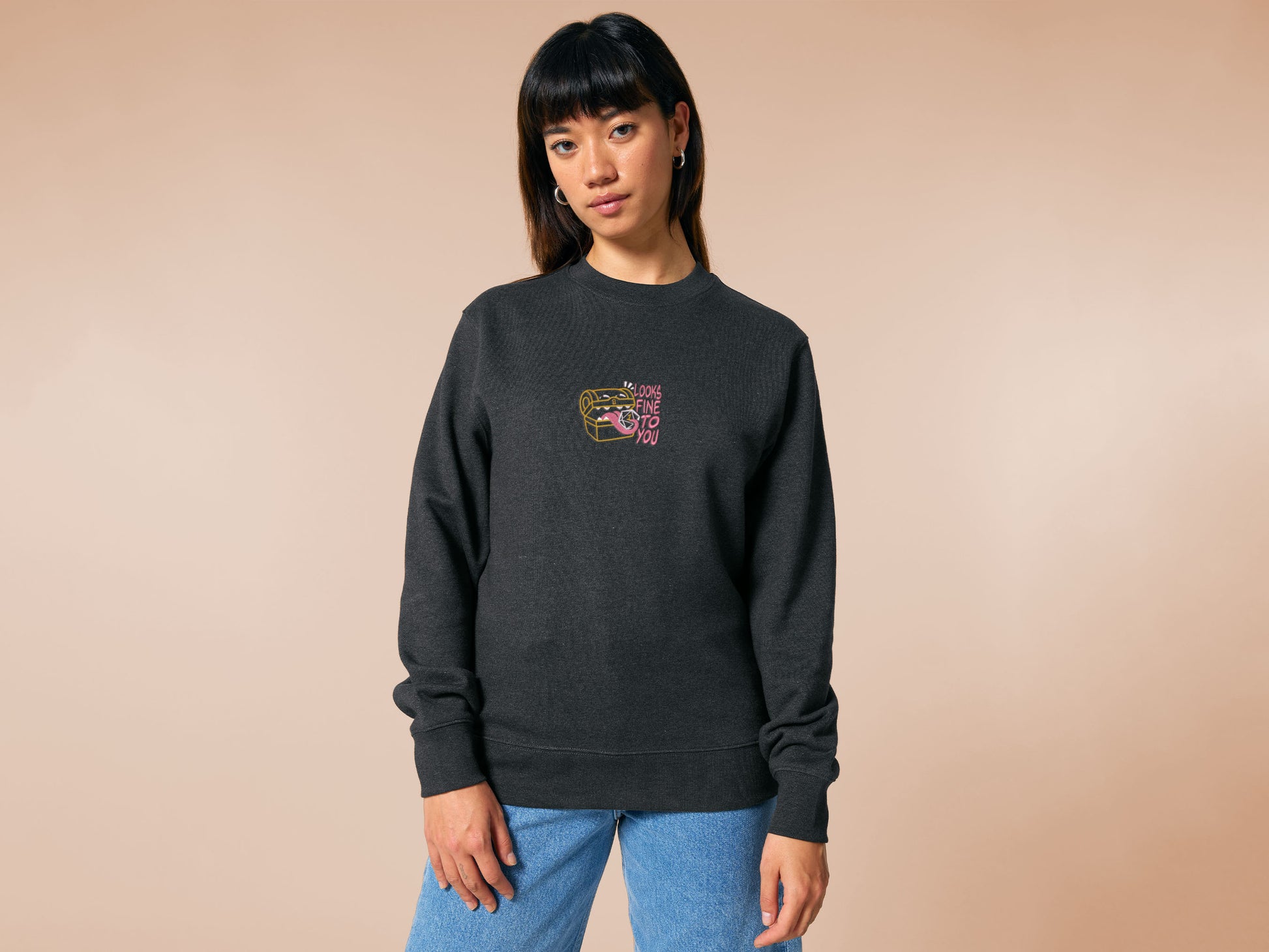 A dark grey crew neck long sleeve sweater, with an embroidered cute chibi mimic chest holding a D20 dice rolled a one and the quote Looks fine to you.