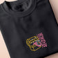 A dark grey crew neck short sleeve t-shirt, with an embroidered cute chibi mimic chest holding a D20 dice rolled a one and the quote Looks fine to you.