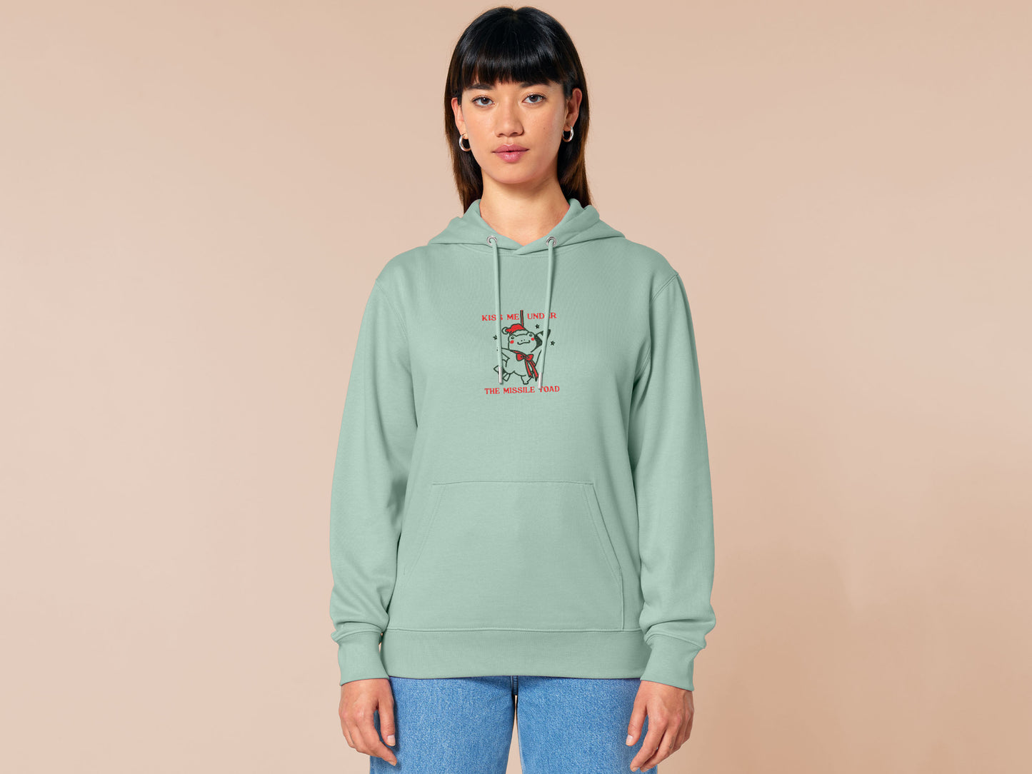 Green Christmas jumper hoodie with an embroidered design of the viral frog
meme Missile Toad, featuring a cute hanging chibi Christmas frog with the quote kiss me under the missile toad