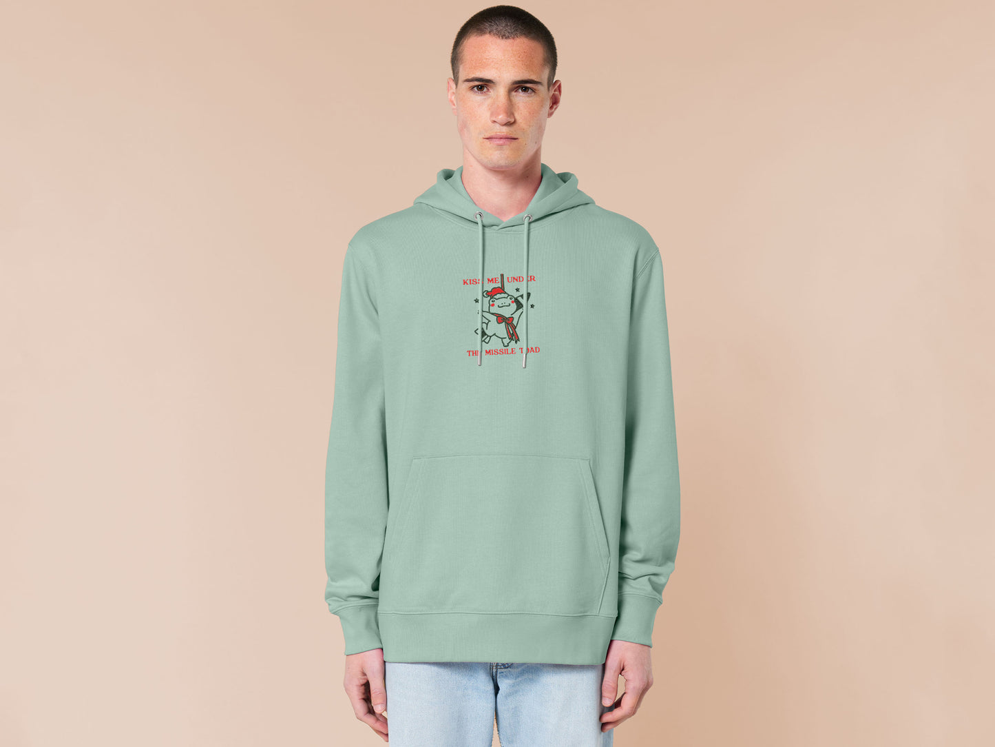 Green Christmas jumper hoodie with an embroidered design of the viral frog
meme Missile Toad, featuring a cute hanging chibi Christmas frog with the quote kiss me under the missile toad