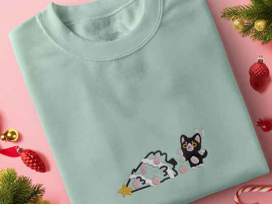 Green Christmas jumper with an embroidered design of a cute black cat shocked at a fallen down christmas tree that they clearly pushed over