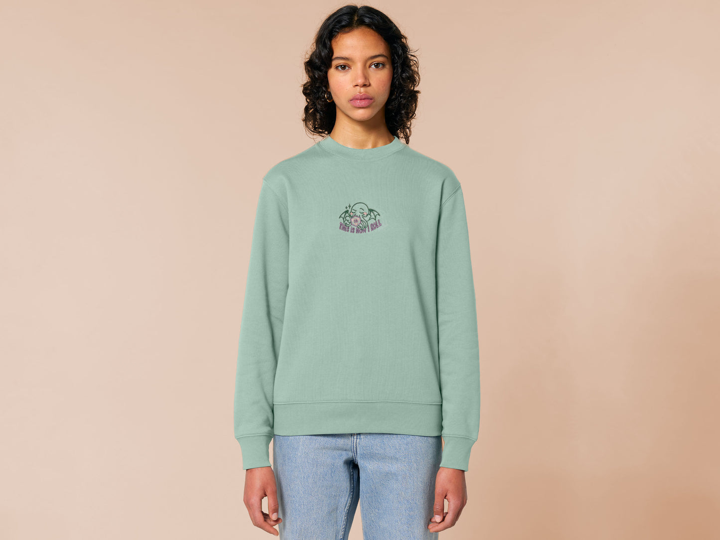 An embroidered green sweater design of a cute Cthullu with a D20 dice surrounded by the quote This Is How I Roll