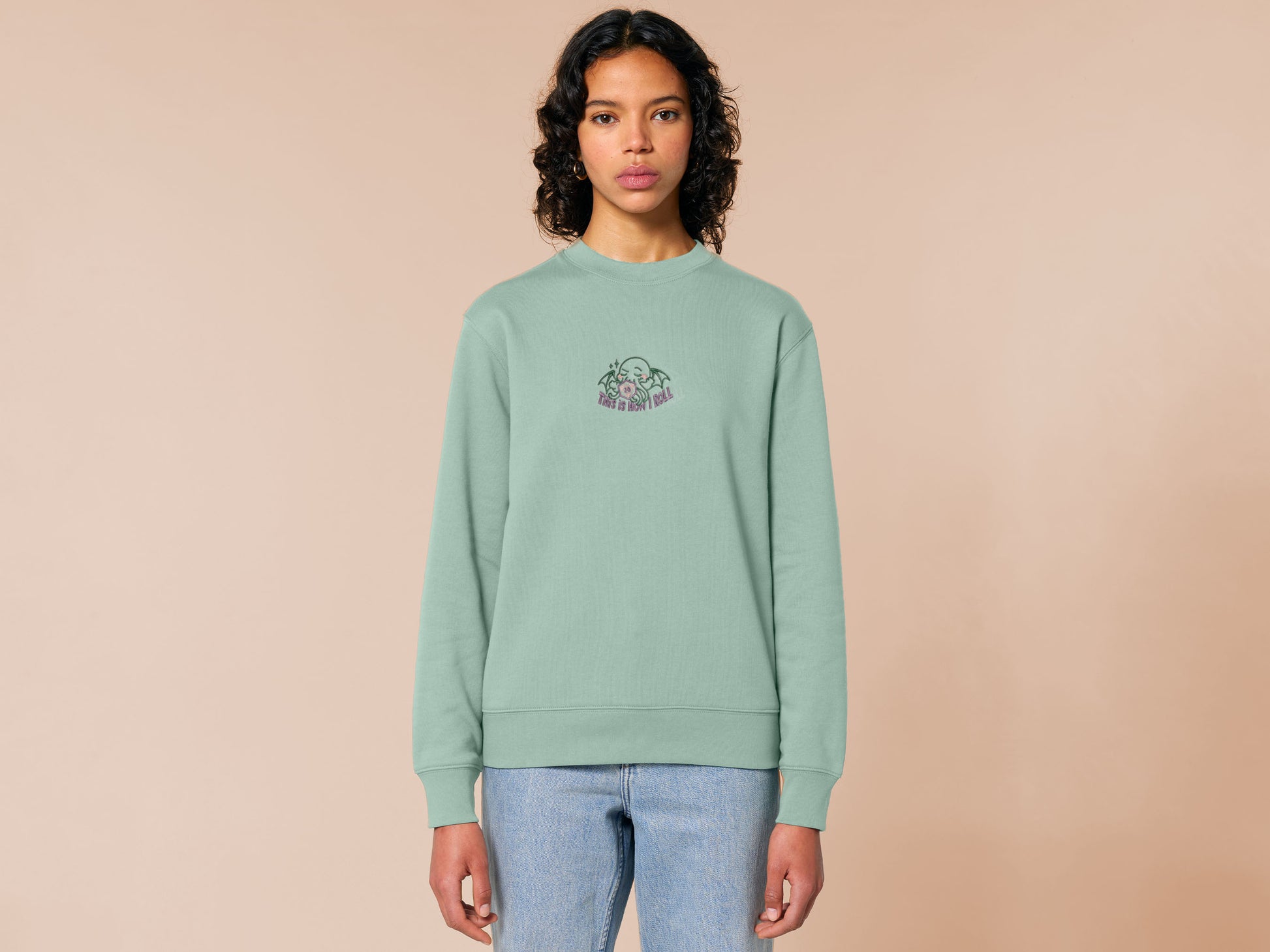 An embroidered green sweater design of a cute Cthullu with a D20 dice surrounded by the quote This Is How I Roll