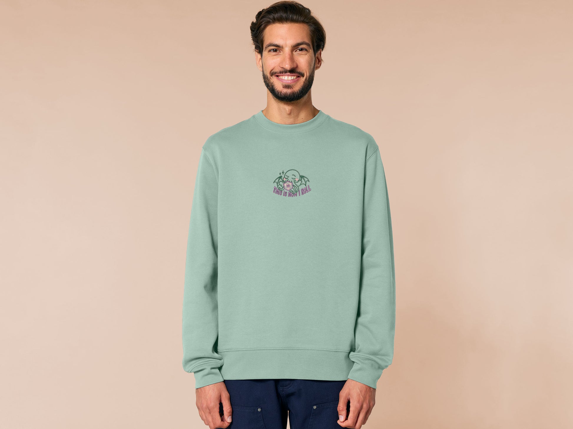 An embroidered green sweater design of a cute Cthullu with a D20 dice surrounded by the quote This Is How I Roll