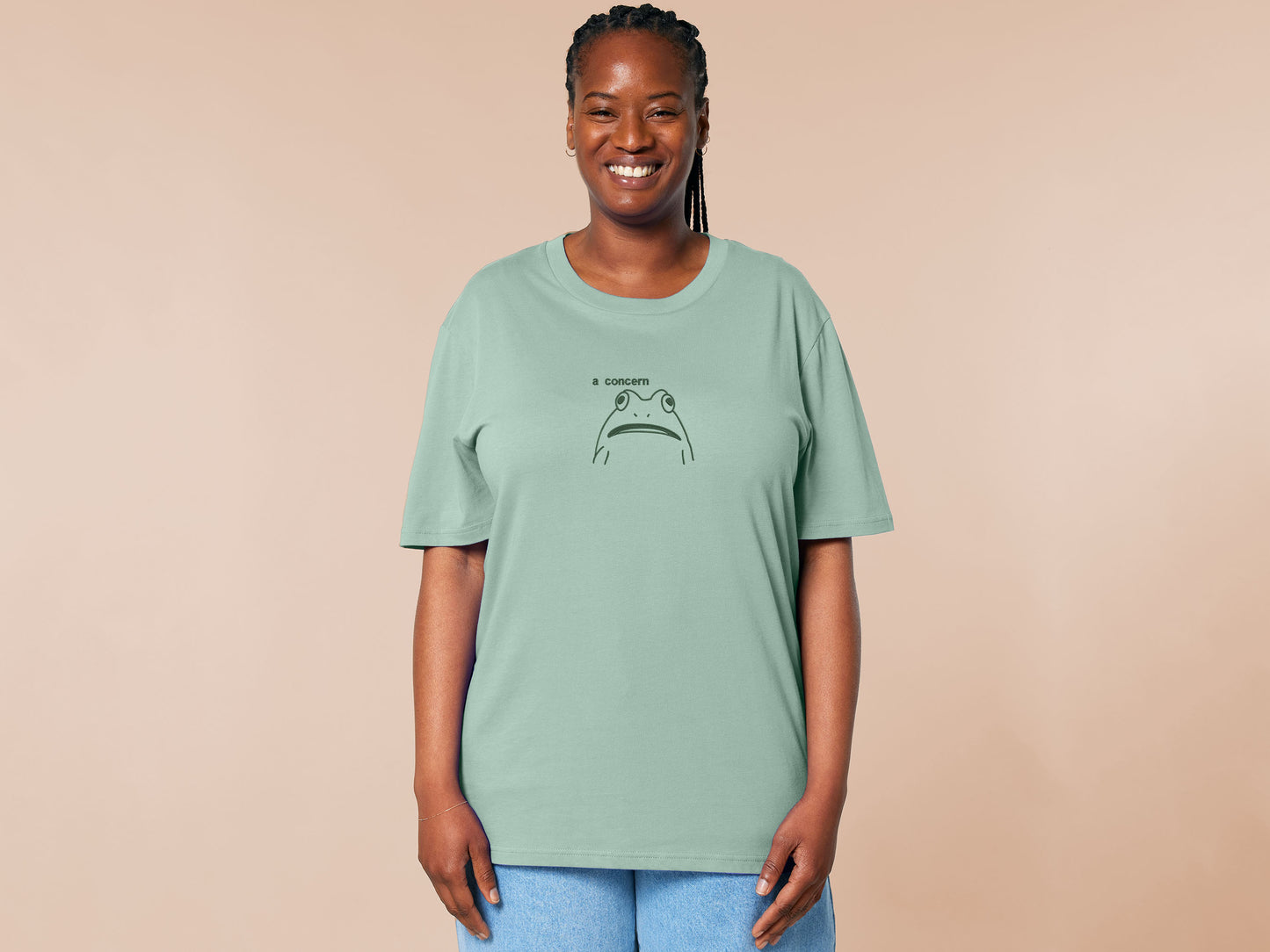 An embroidered green t-shirt design of a funny cartoon frog with the text a concern.