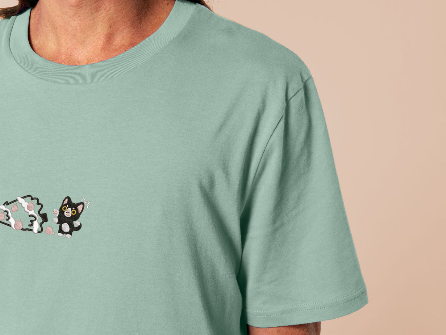 Green Christmas tshirt with an embroidered design of a cute black cat shocked at a fallen down christmas tree that they clearly pushed over