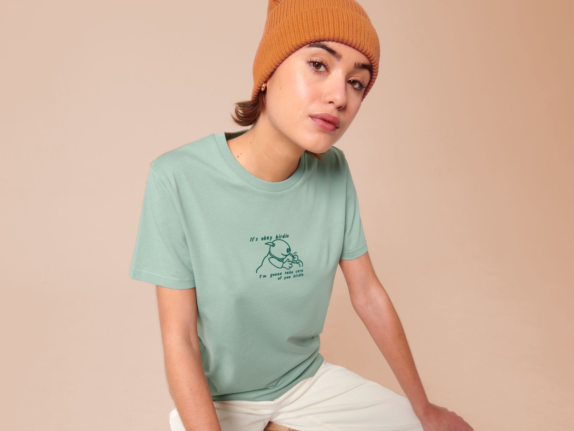 Woman wearing a green embroidered short sleeved t-shirt design of Mona from Nanalan comforting Birdie with the text It's okay Birdie I'm gonna take care of you birdie