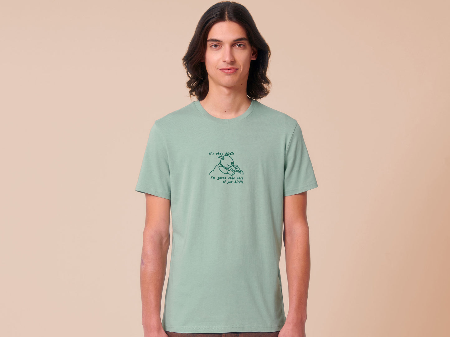 Man wearing a green embroidered short sleeved t-shirt design of Mona from Nanalan comforting Birdie with the text It's okay Birdie I'm gonna take care of you birdie