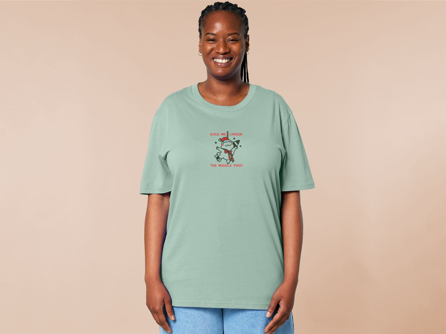 Green Christmas jumper t-shirt with an embroidered design of the viral frog
meme Missile Toad, featuring a cute hanging chibi Christmas frog with the quote kiss me under the missile toad