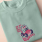 An embroidered green t-shirt design of a cute clown frog wearing a party hat and driving a toy car surrounded by the quote on my way to make things worse!