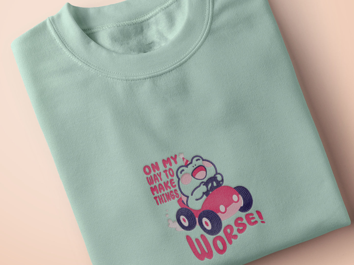 An embroidered green t-shirt design of a cute clown frog wearing a party hat and driving a toy car surrounded by the quote on my way to make things worse!