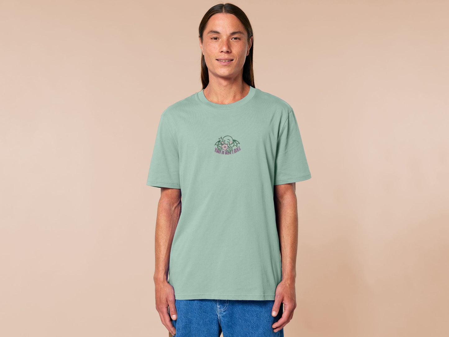 An embroidered green t-shirt design of a cute Cthullu with a D20 dice surrounded by the quote This Is How I Roll