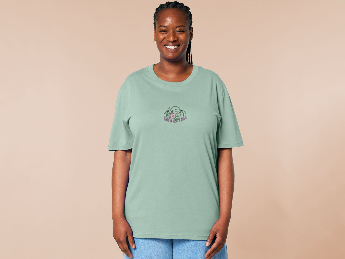 An embroidered green t-shirt design of a cute Cthullu with a D20 dice surrounded by the quote This Is How I Roll
