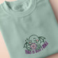 An embroidered green t-shirt design of a cute Cthullu with a D20 dice surrounded by the quote This Is How I Roll