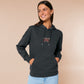 A dark grey long sleeve hoodie, with an embroidered chibi mothman and the quote Live Lamp Lurk.