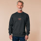 A dark grey crew neck long sleeve sweater, with an embroidered chibi mothman and the quote Live Lamp Lurk.