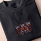 A dark grey crew neck short sleeve t-shirt, with an embroidered chibi mothman and the quote Live Lamp Lurk.