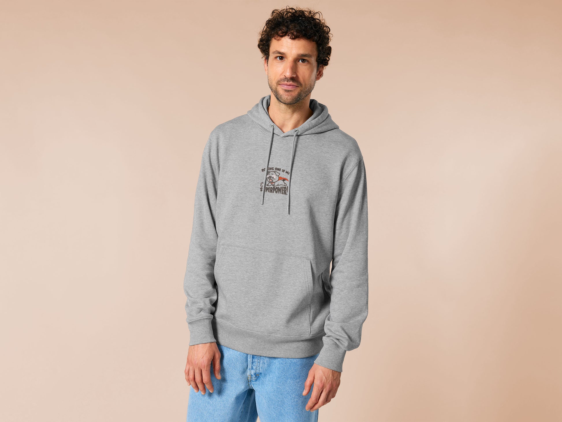 An Embroidered light grey hoodie design of a cute chibsuper dog wearing a red cape panicked at a dice with the text rolling one is my superpower