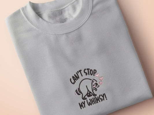 An Embroidered light grey t-shirt design of a cute Jimothy the viral disabled raccoon and the quote can't stop my whimsy!