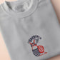 An Embroidered light grey t-shirt design of a cute chib french snail with the quote sacreblu!