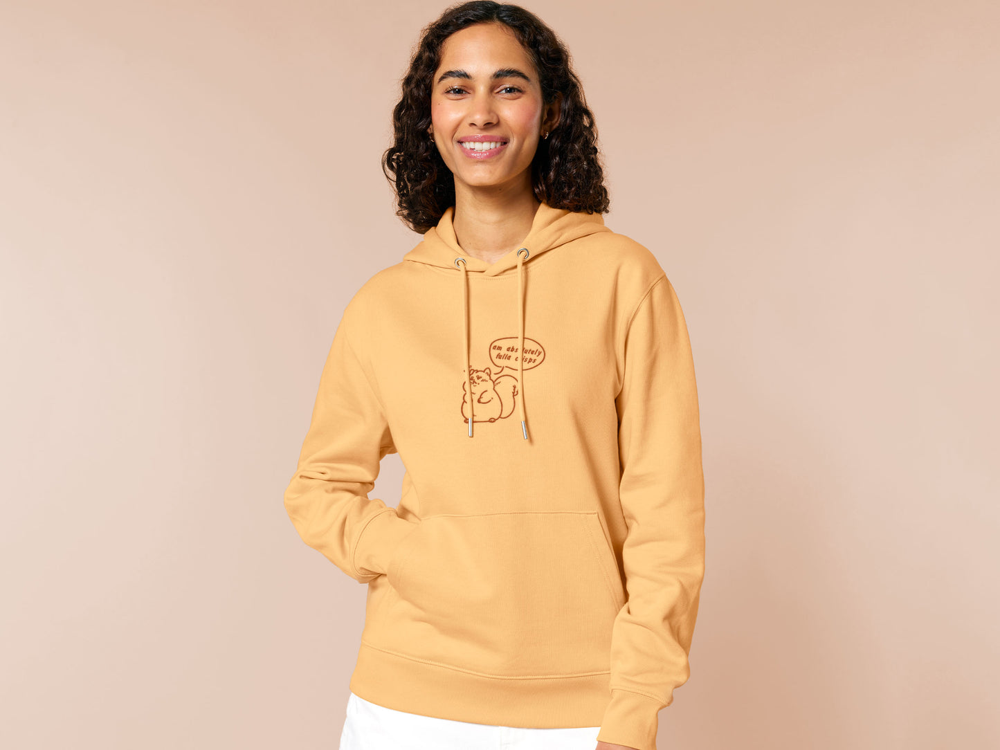 A woman wearing a long sleeved yellow fleece hoodie with an embroidered design of a cute fat squirrel and a speech bubble with the text am absolutely fulla crisps
