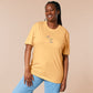 A yellow t-shirt with a blue and pink embroidered design of a cute smiling dinosaur looking at a meteor plummeting to earth with the text uh oh...