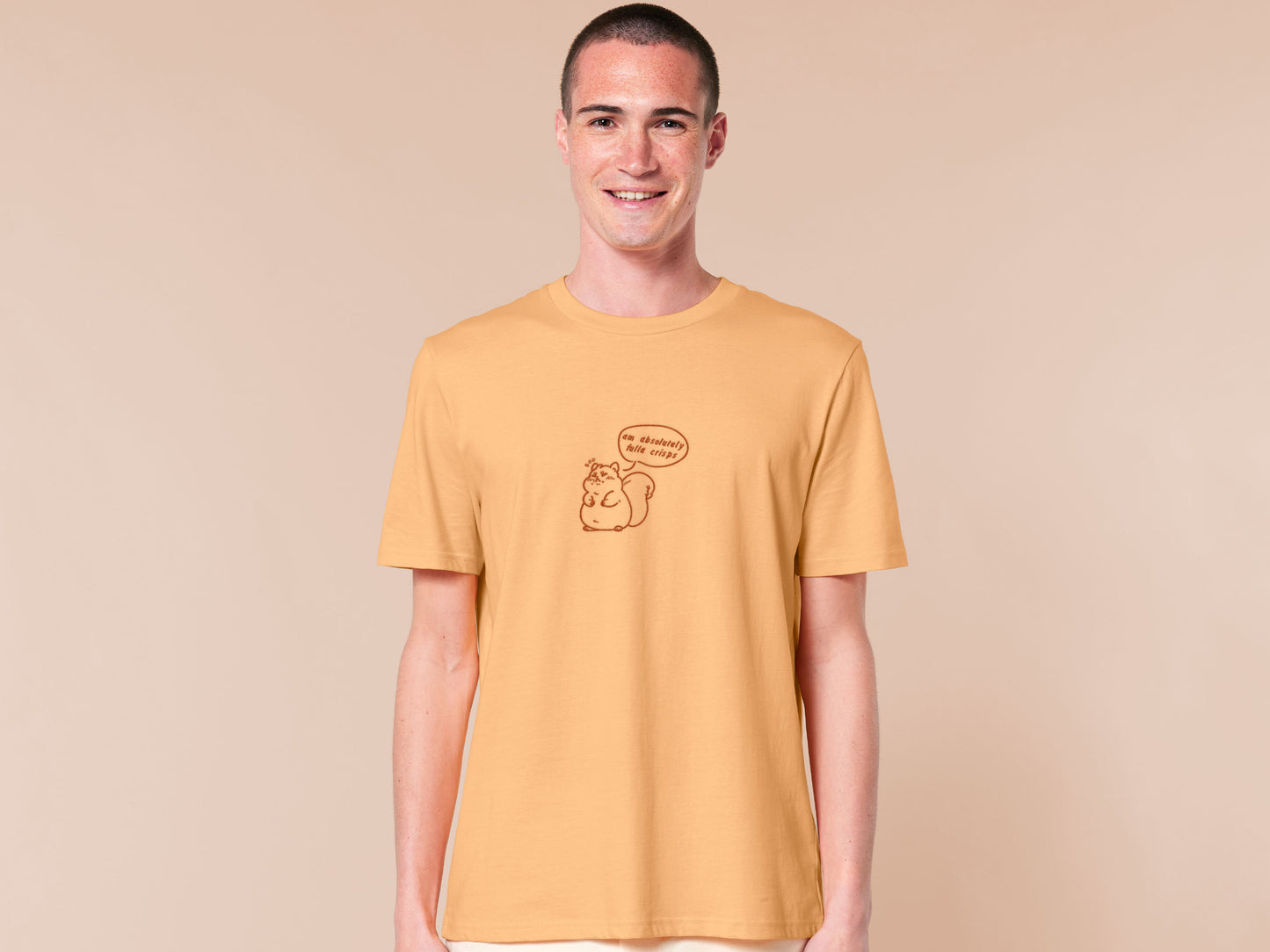A man wearing a short sleeved yellow t-shirt with an embroidered design of a cute fat squirrel and a speech bubble with the text am absolutely fulla crisps