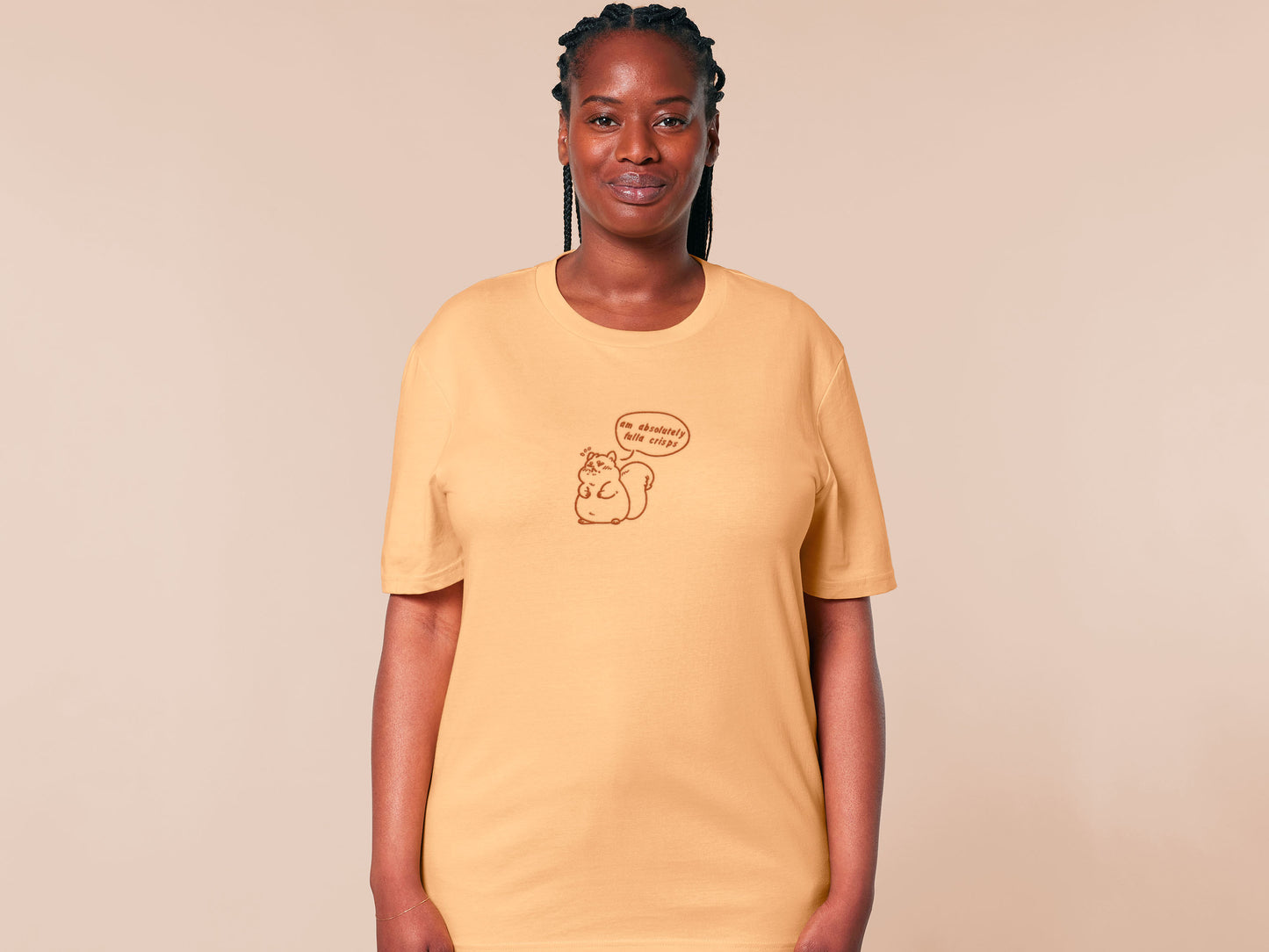 A woman wearing a short sleeved yellow t-shirt with an embroidered design of a cute fat squirrel and a speech bubble with the text am absolutely fulla crisps