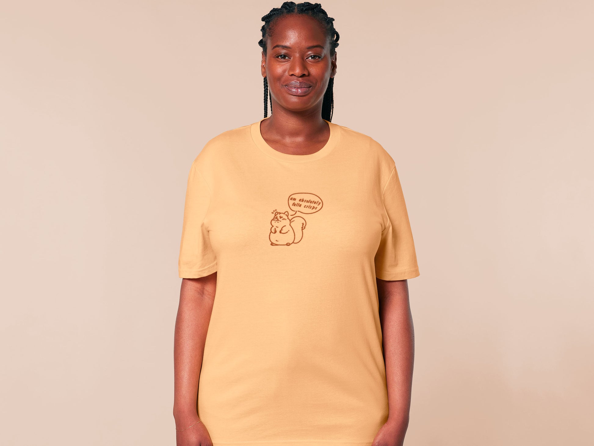 A woman wearing a short sleeved yellow t-shirt with an embroidered design of a cute fat squirrel and a speech bubble with the text am absolutely fulla crisps