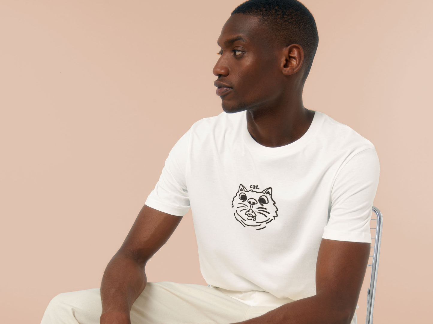 Man wearing a short sleeved white t-shirt with an Embroidered cat design