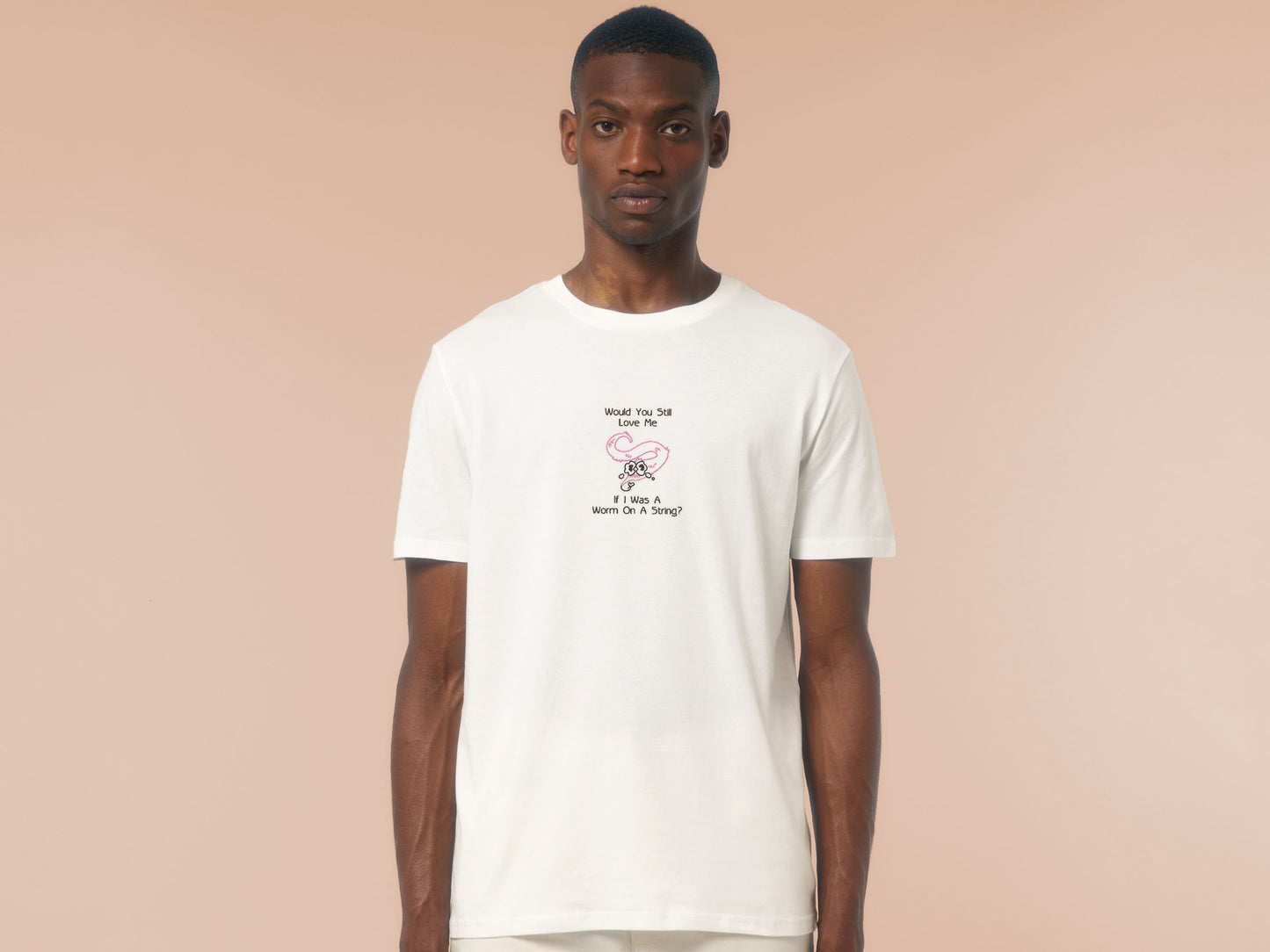 A man wearing an off white short sleeved crew neck t-shirt with an embroidered design of a pink worm on a string with a cute face crying with the black text Would You Still Love Me If I Was A Worm On A String