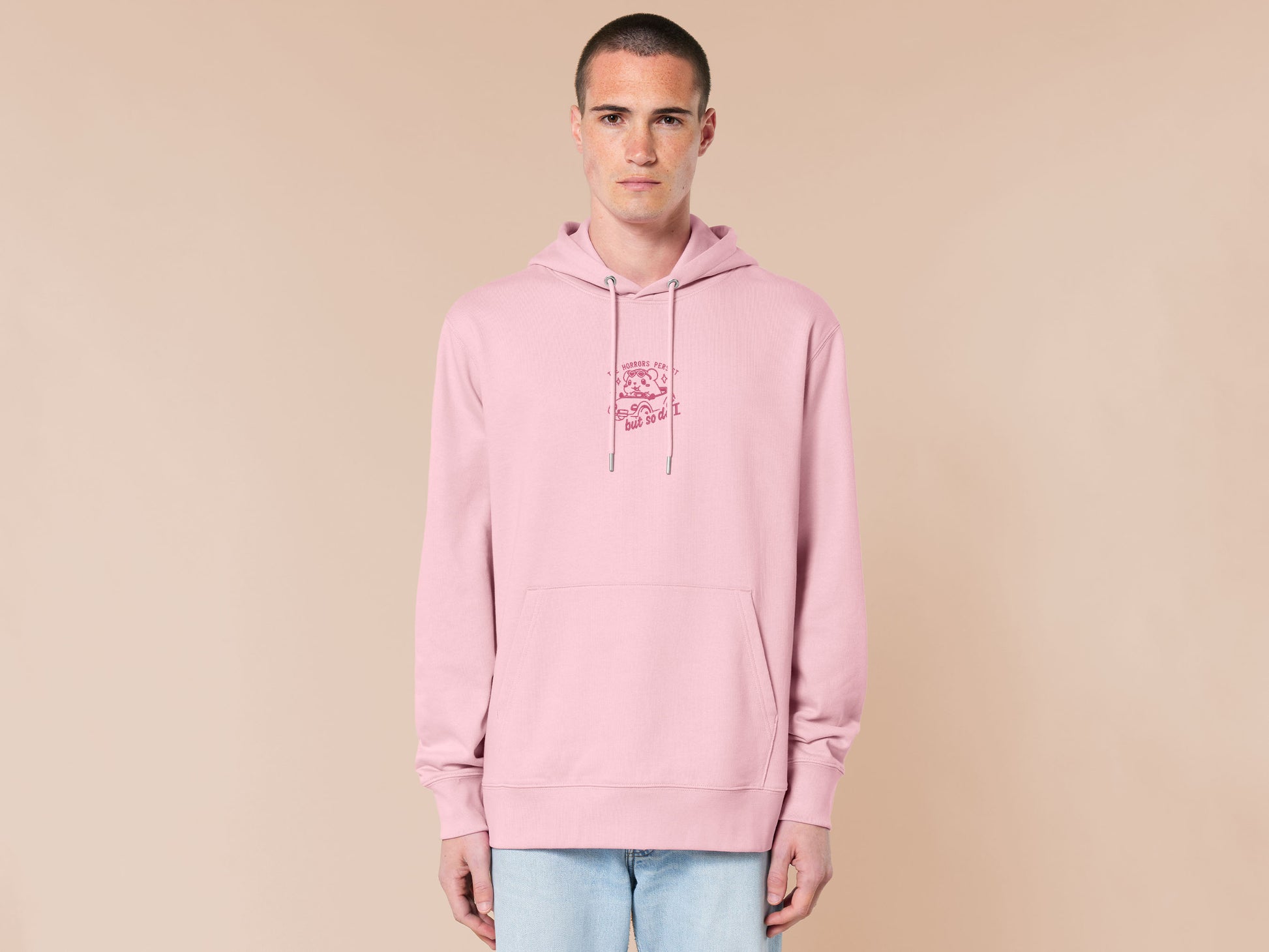 Pink embroidered hoodie with a cute chibi guinea pig hamster wearing heart-shaped sunglasses and driving a little pink car surrounded by the quote the horrors persist but so do I.