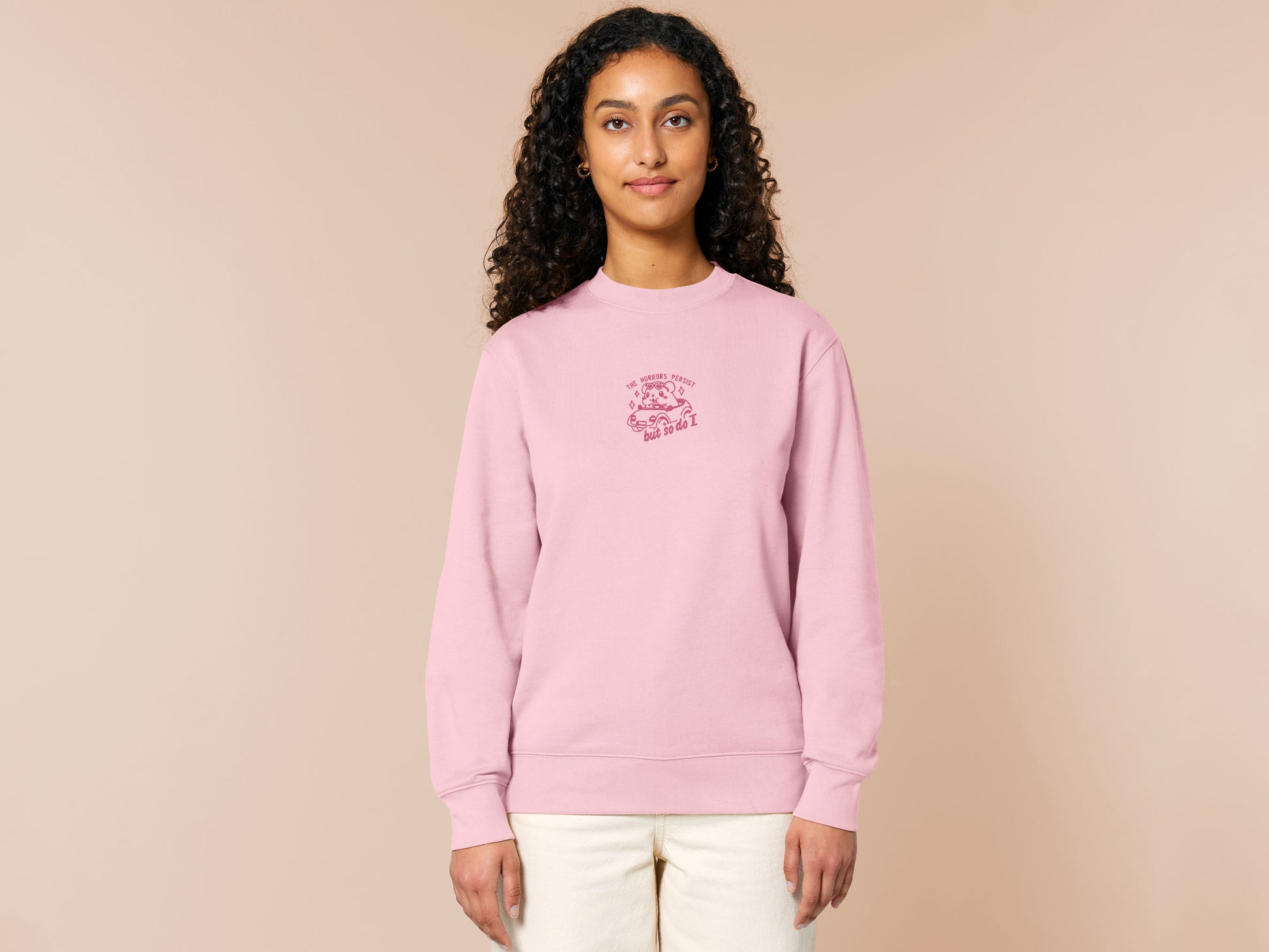 Pink embroidered sweater with a cute chibi guinea pig hamster wearing heart-shaped sunglasses and driving a little pink car surrounded by the quote the horrors persist but so do I.